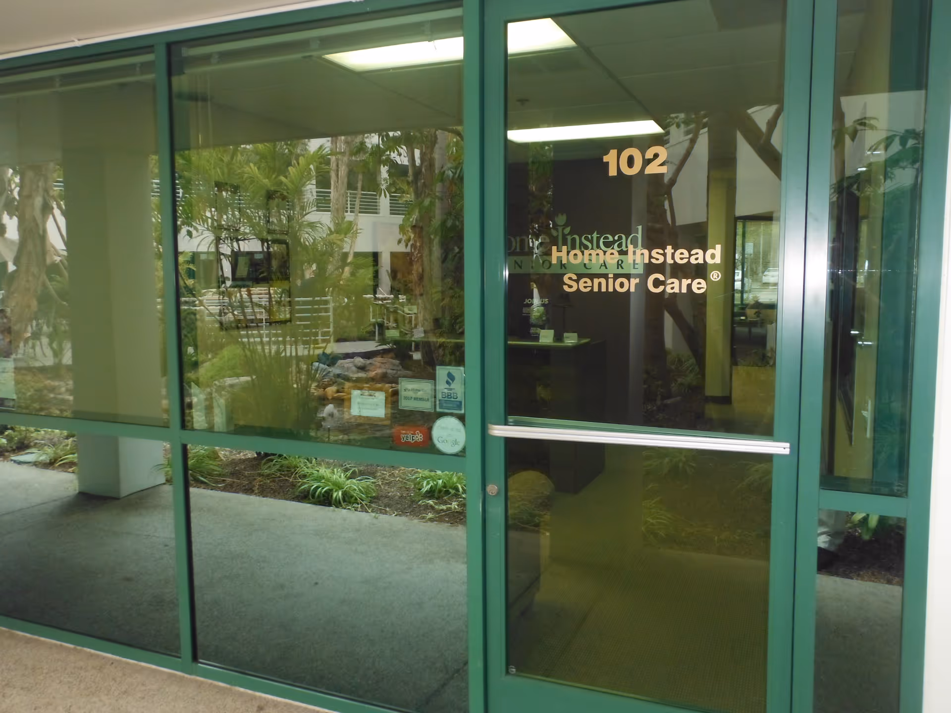 Green-framed glass entrance door with Home Instead Senior Care signage, lobby visible inside.