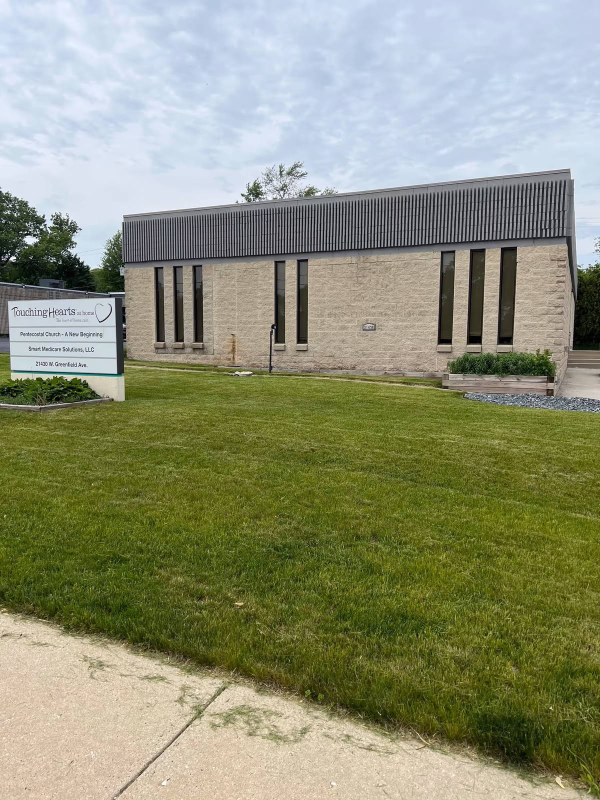 Modern brick facility front with tall vertical windows and a Touching Hearts At Home sign.