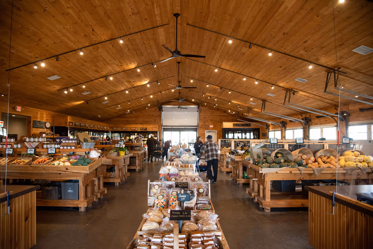 Wood-paneled indoor market hall with produce displays and shoppers browsing aisles.