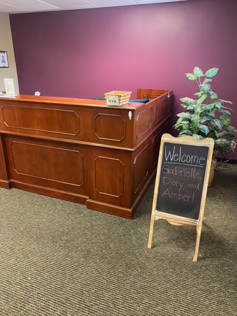 Reception desk in burgundy lobby with a plant and chalkboard welcome sign.