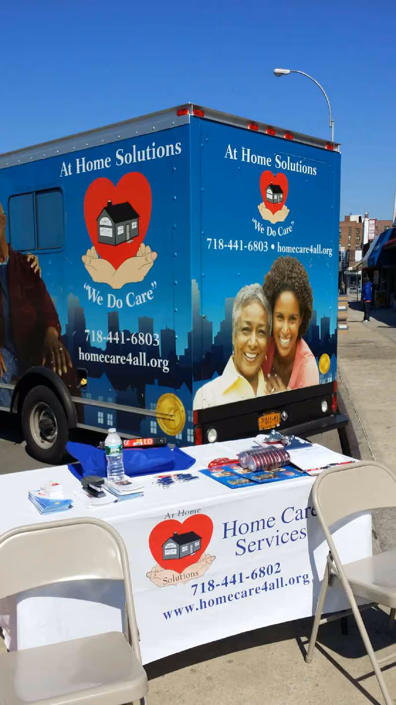 Blue promotional At Home Solutions van parked outdoors beside a brochure table.