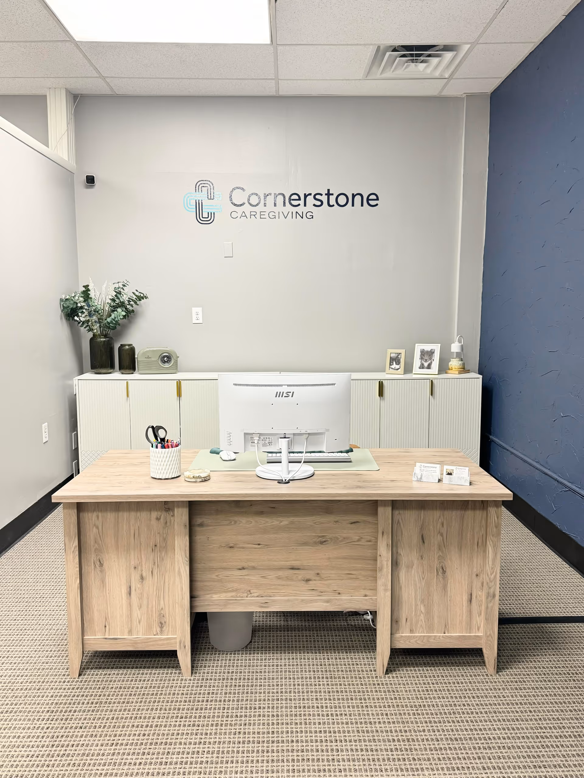 Reception area with a wooden desk, computer, and Cornerstone Caregiving logo on wall.