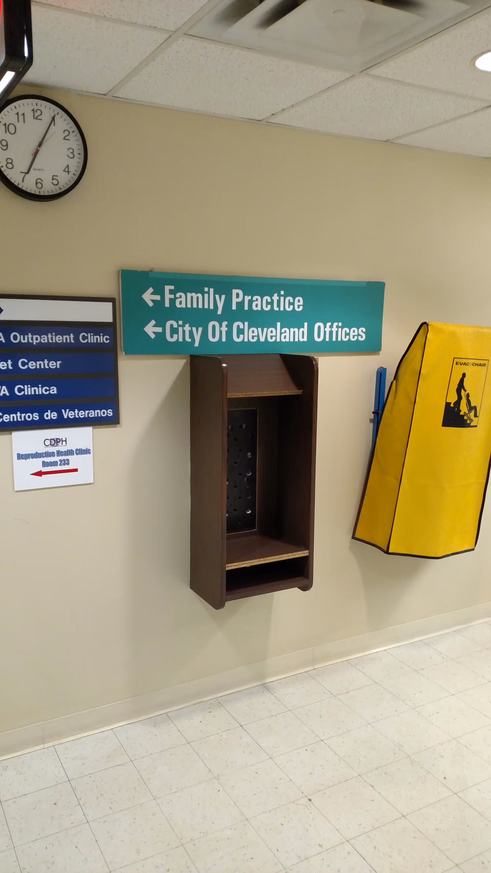 Interior hallway with clock, teal directional sign, empty wall shelf, and yellow evacuation chair.