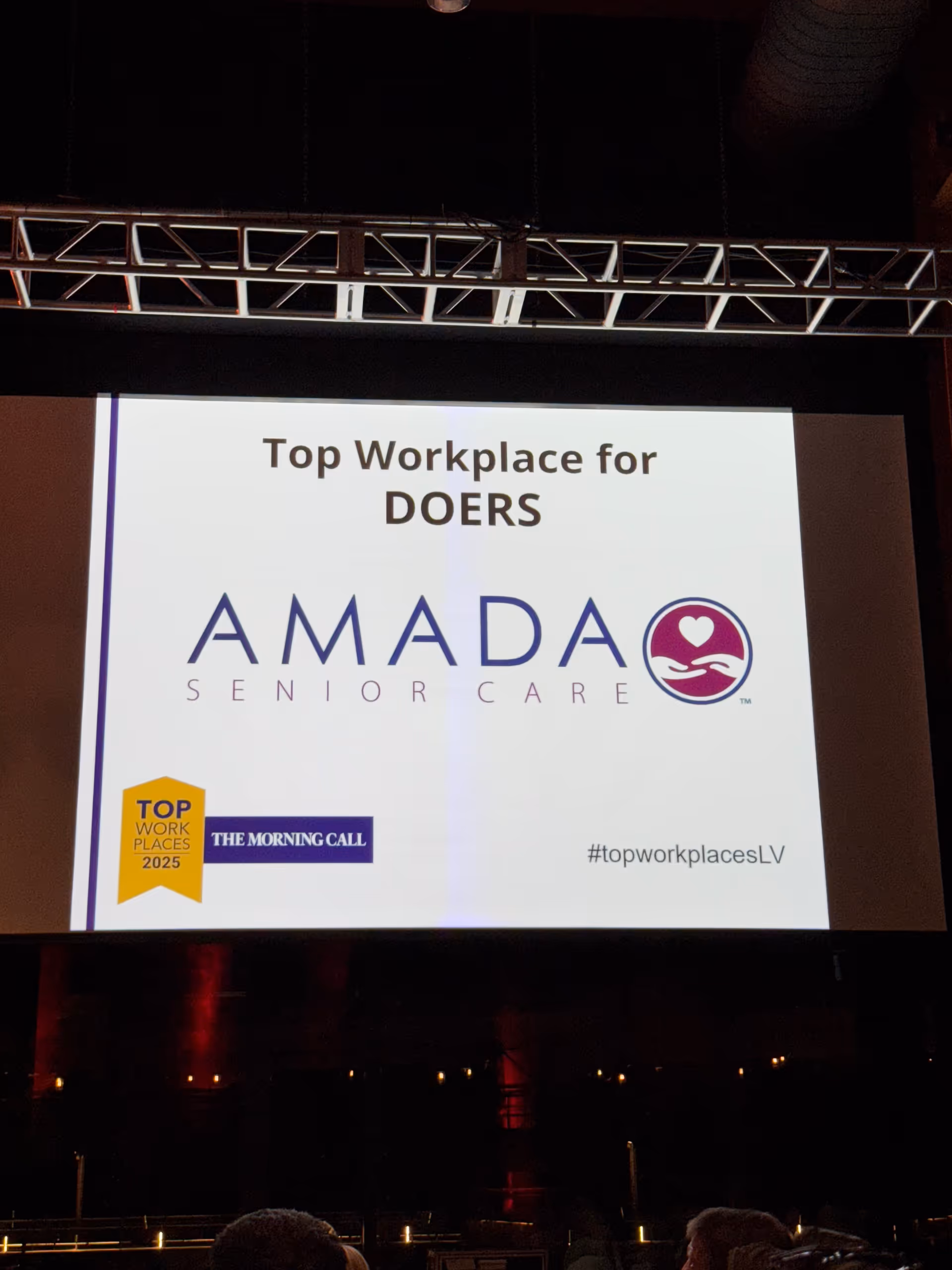 A presentation slide on a large screen promoting Amada Senior Care at an event.