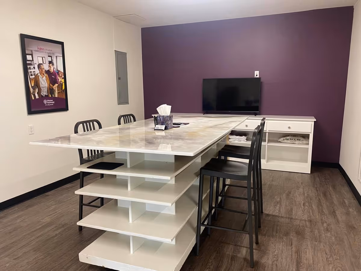 A modern communal dining area with a marble-topped island table, stools, a TV, and purple wall.