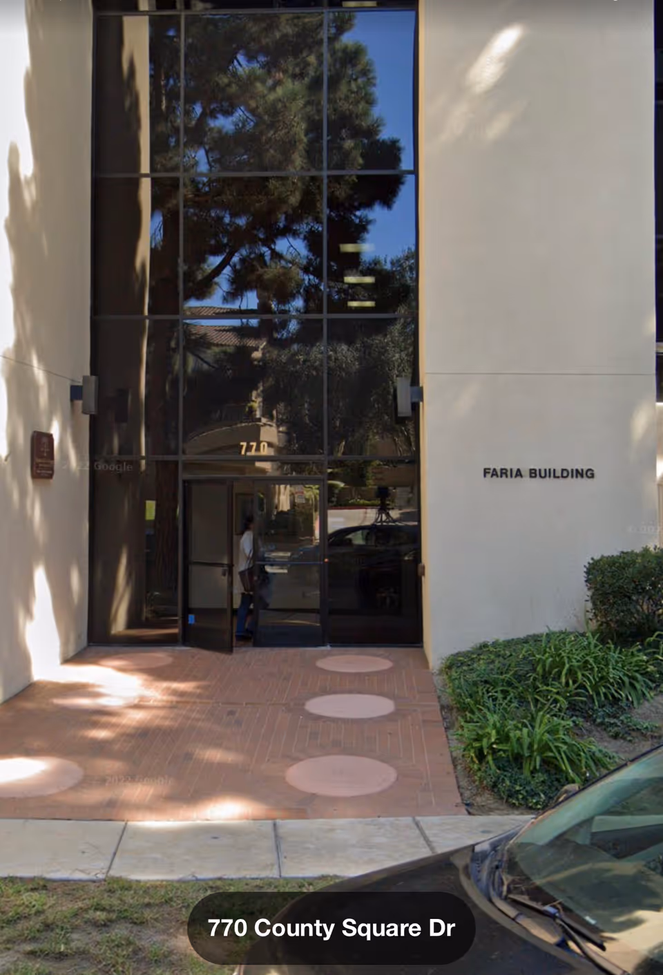 Front view of a building entrance with glass doors and landscaping.