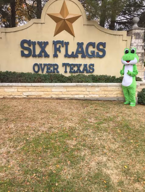 A large Six Flags sign with a green frog mascot outdoors.