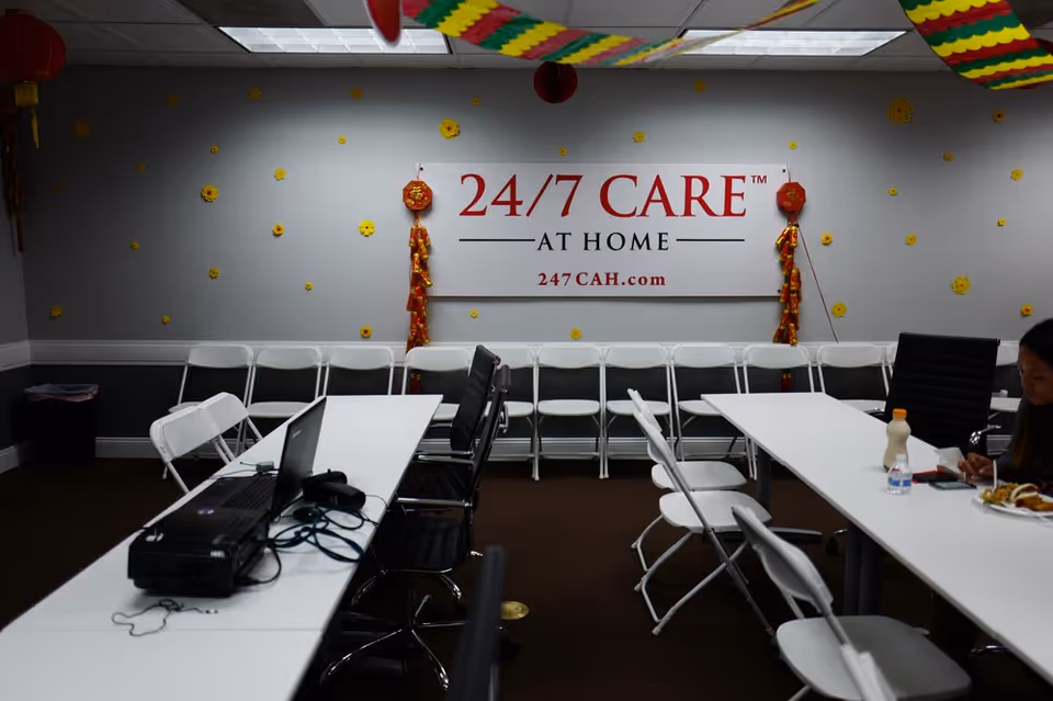 Interior room in a care facility with a prominent 24/7 CARE AT HOME sign and tables.