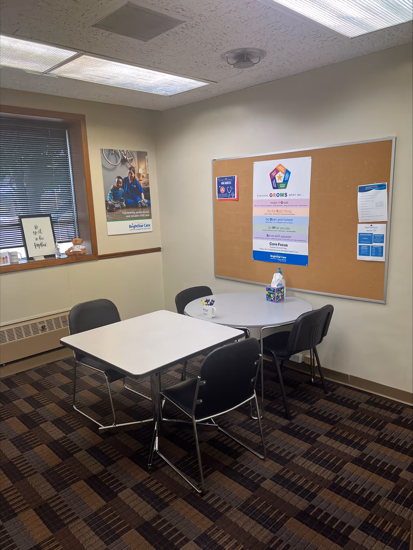 Interior meeting room at BrightStar Care with two white tables, chairs, and a bulletin board.