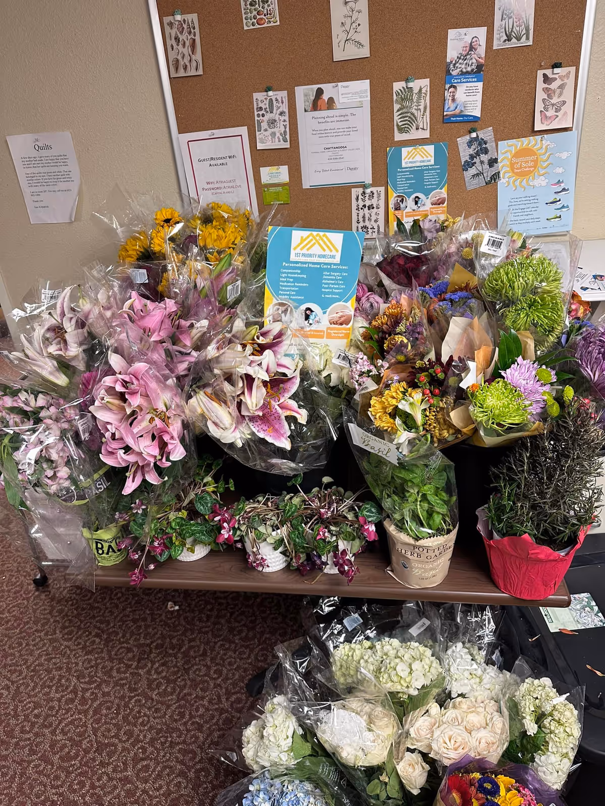 Indoor common area with colorful flower bouquets arranged on a table against bulletin board.