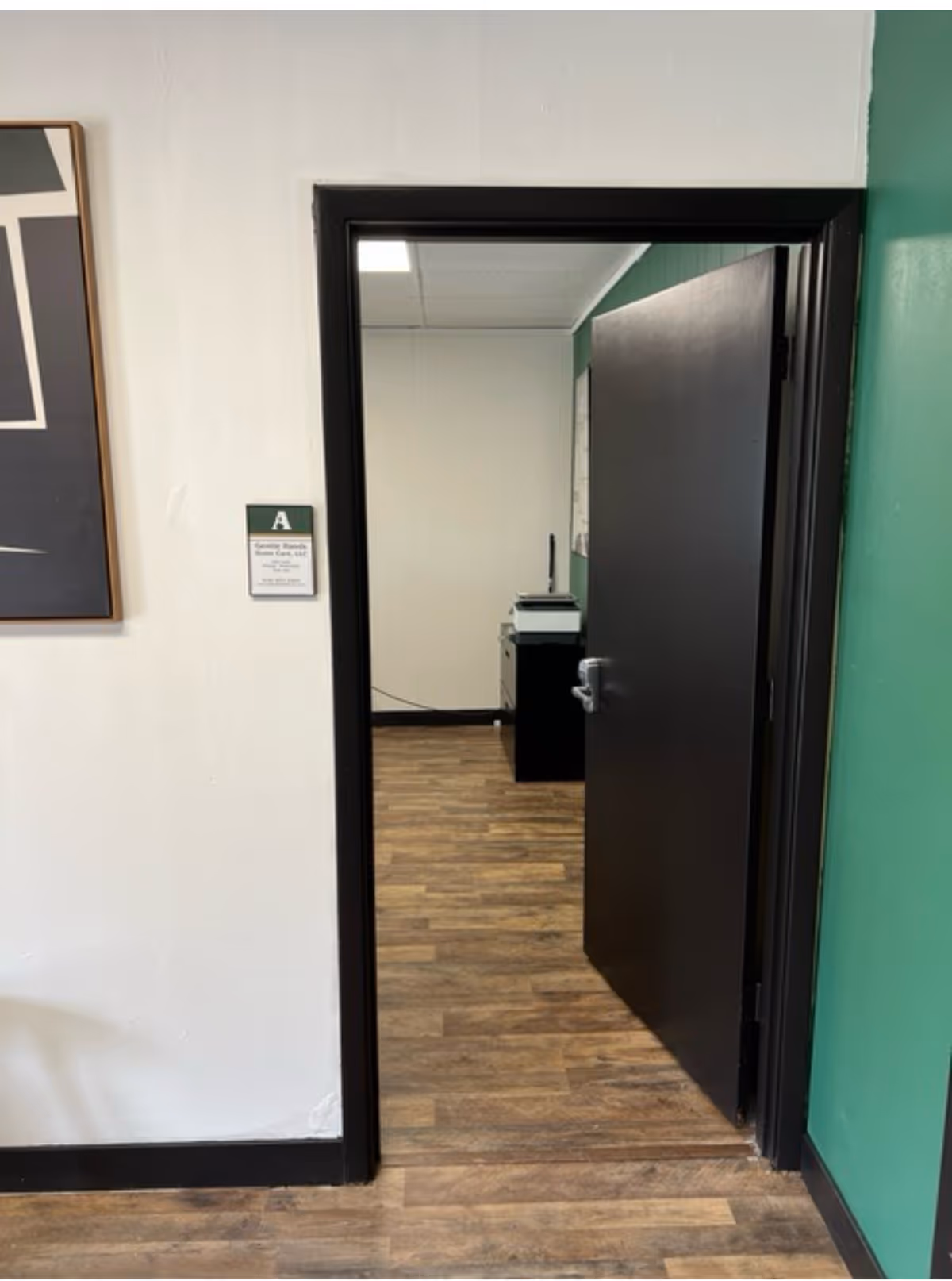 Interior hallway with an open doorway, wooden flooring, green and white walls, a copier visible.