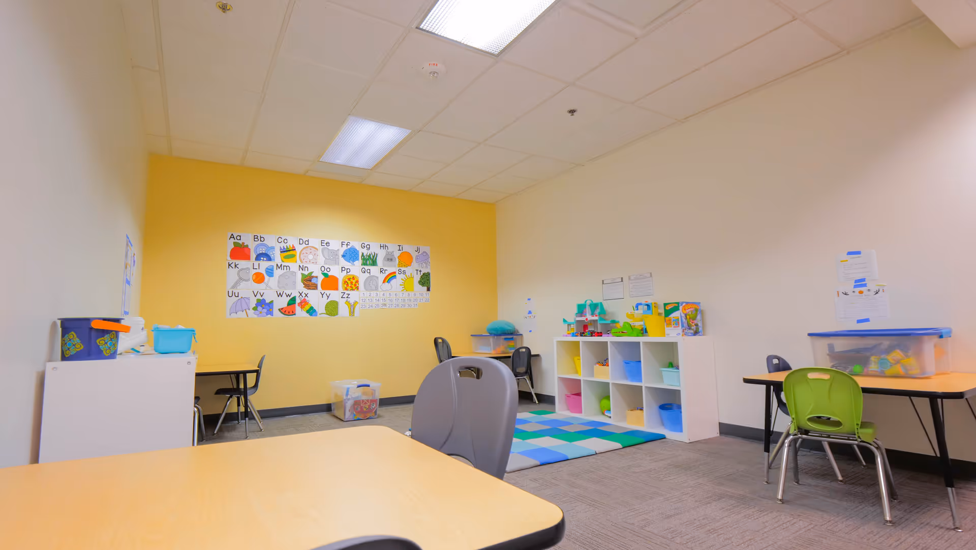 Bright playroom with colorful cubbies, alphabet chart, and child-sized tables.