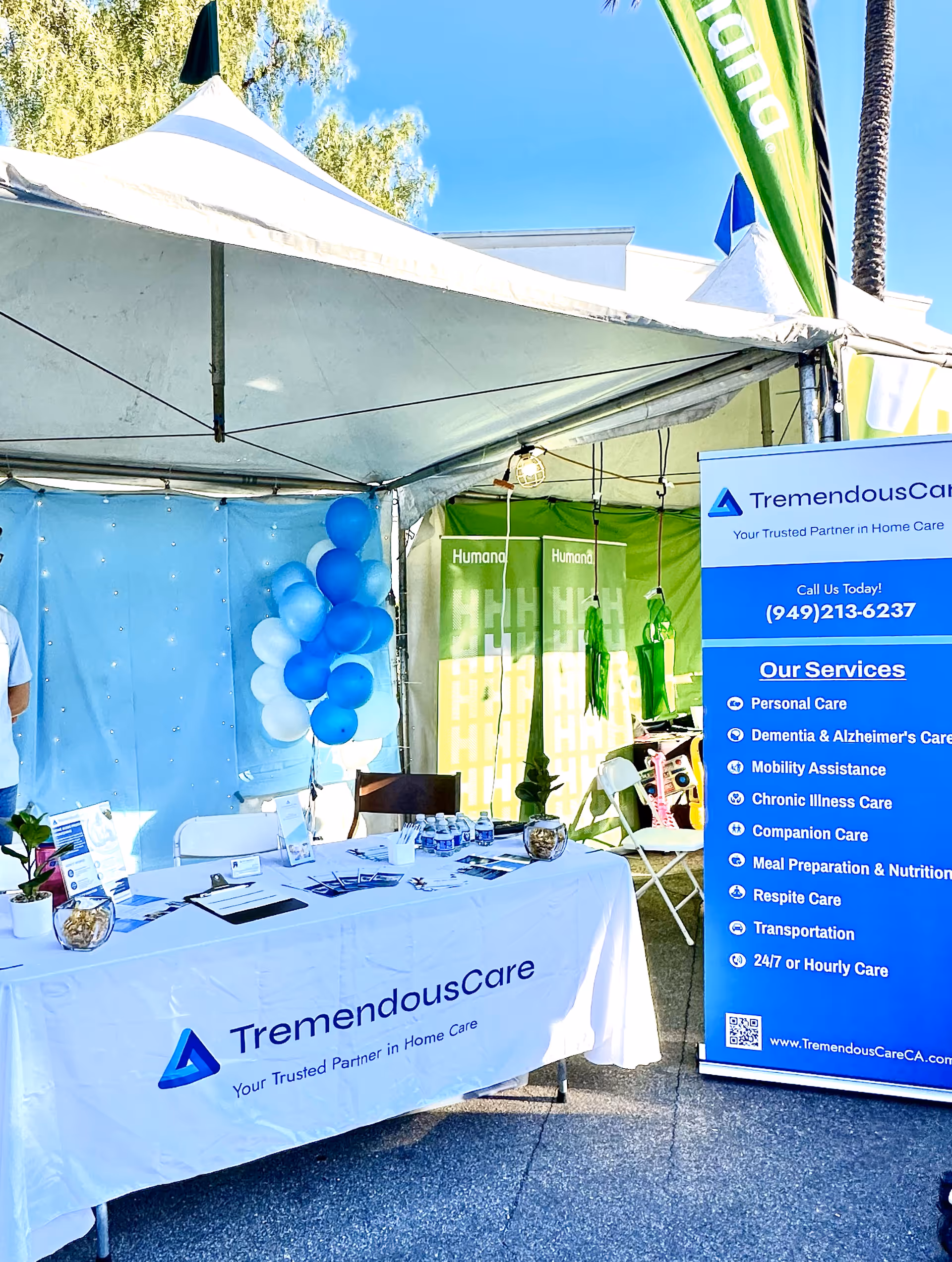 Outdoor TremendousCare booth with blue banners, balloons, and a white table at an event.