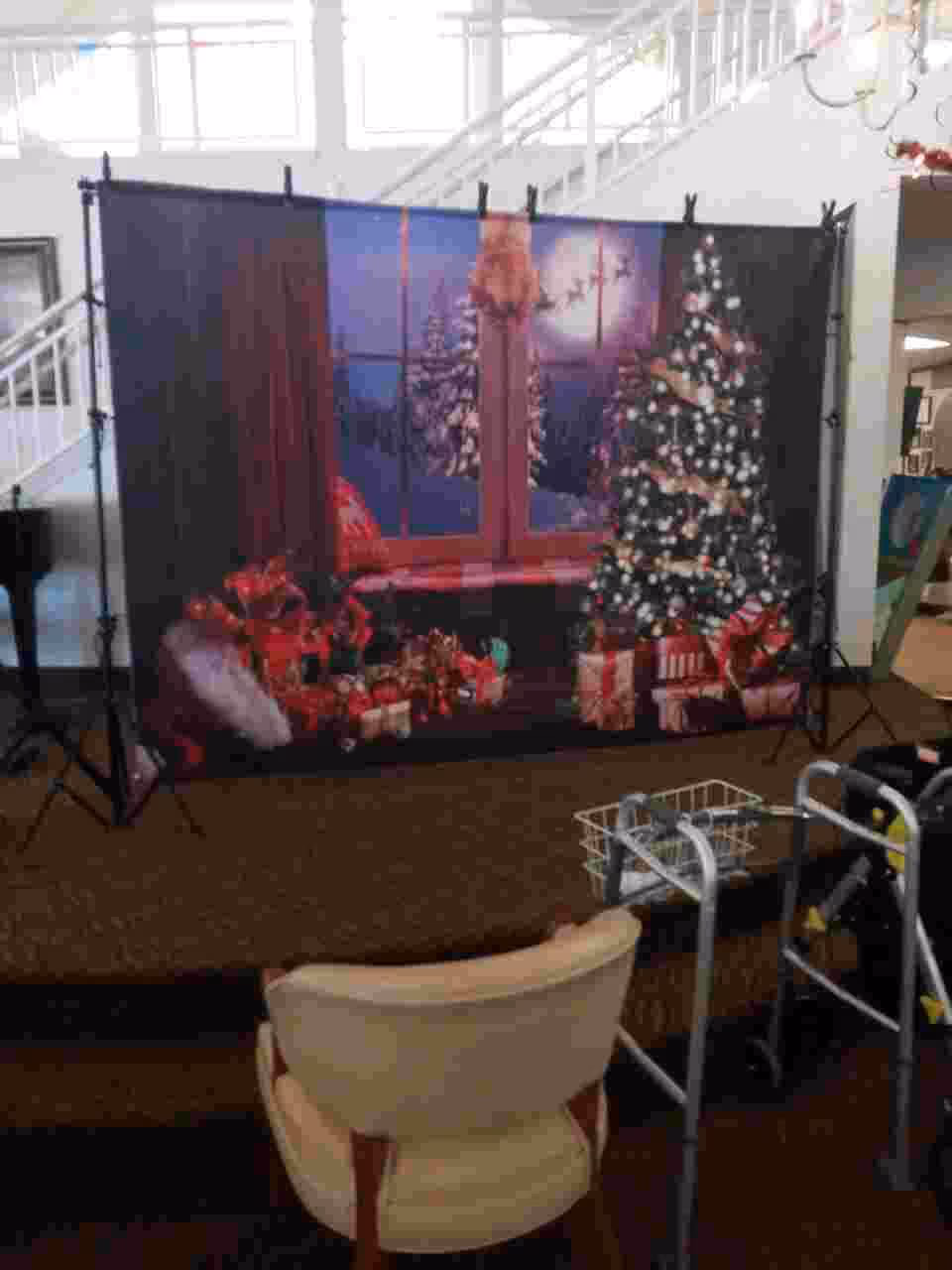 Indoor lounge featuring a Christmas backdrop with tree, gifts, a chair, and a walker.