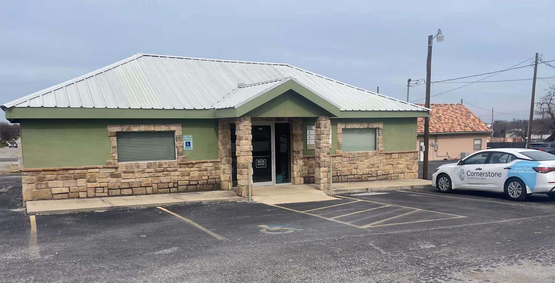 Exterior view of a green, stone-walled Cornerstone Caregiving building with a parked car.