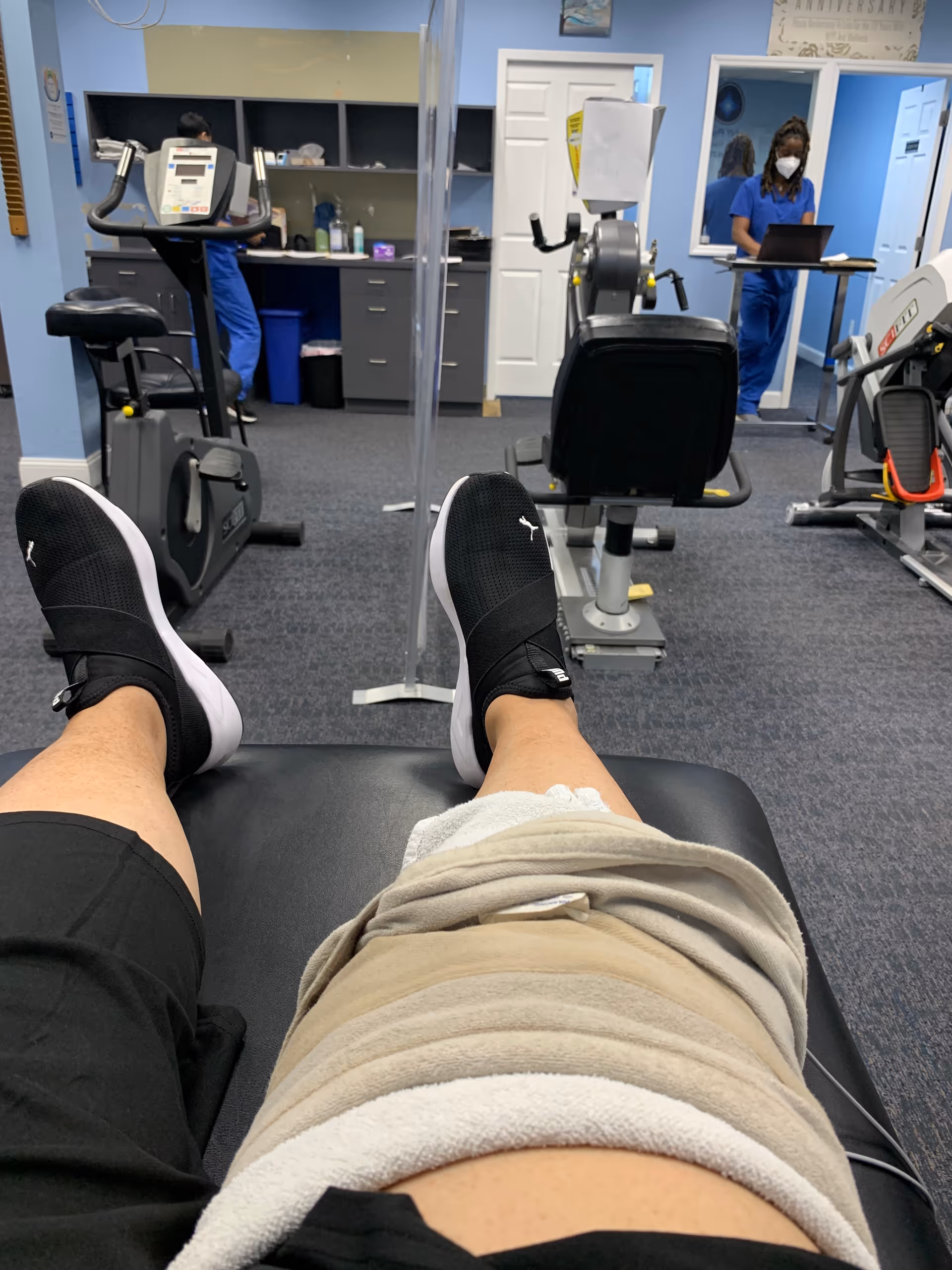 View from a patient's treatment table into a therapy gym with equipment and staff.