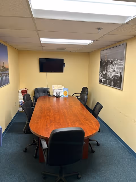 A long wooden conference table with chairs in a yellow-walled meeting room.