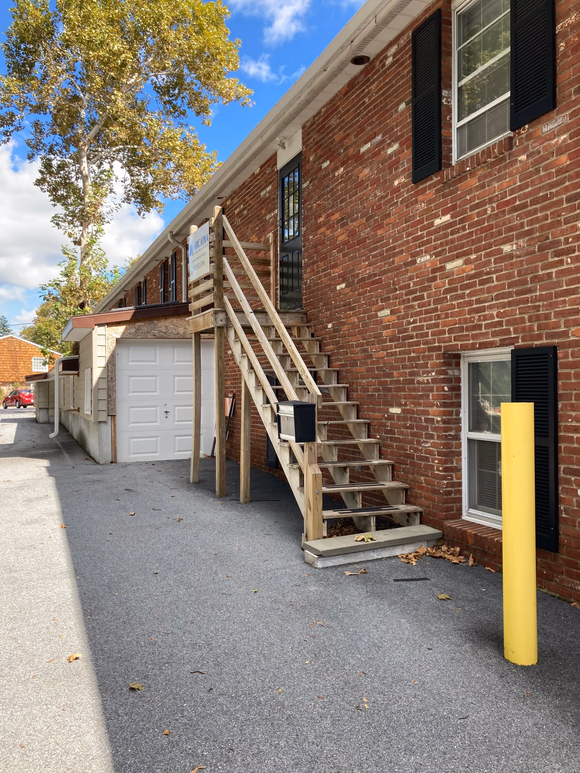 Brick building exterior with wooden stairs, railing, a garage door, and autumn trees.