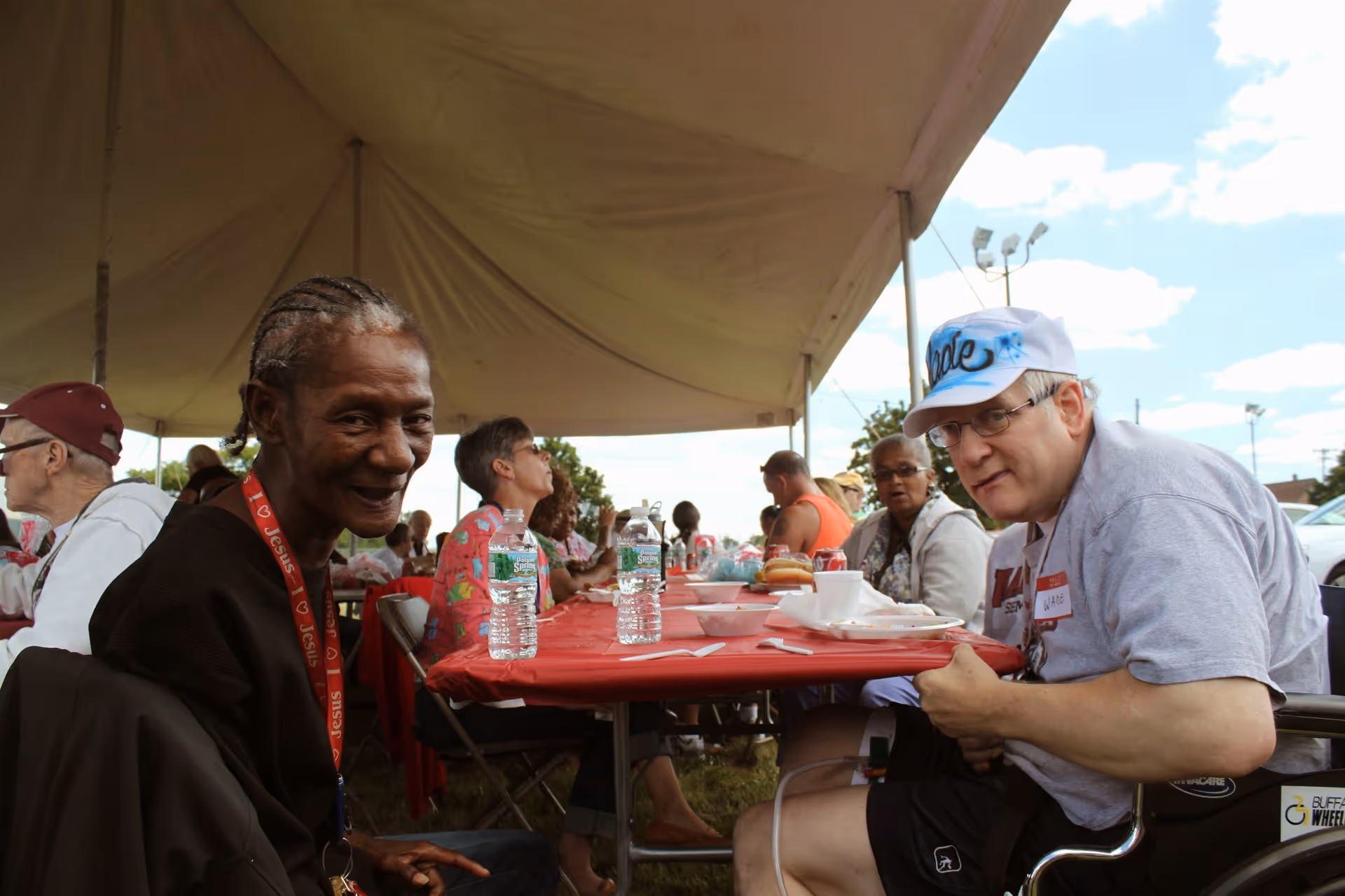 Group of seniors and volunteers dine at an outdoor tented event.