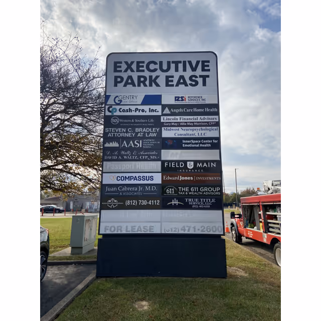 Large outdoor signboard displaying multiple business logos, including Compassus, on a grassy lot.