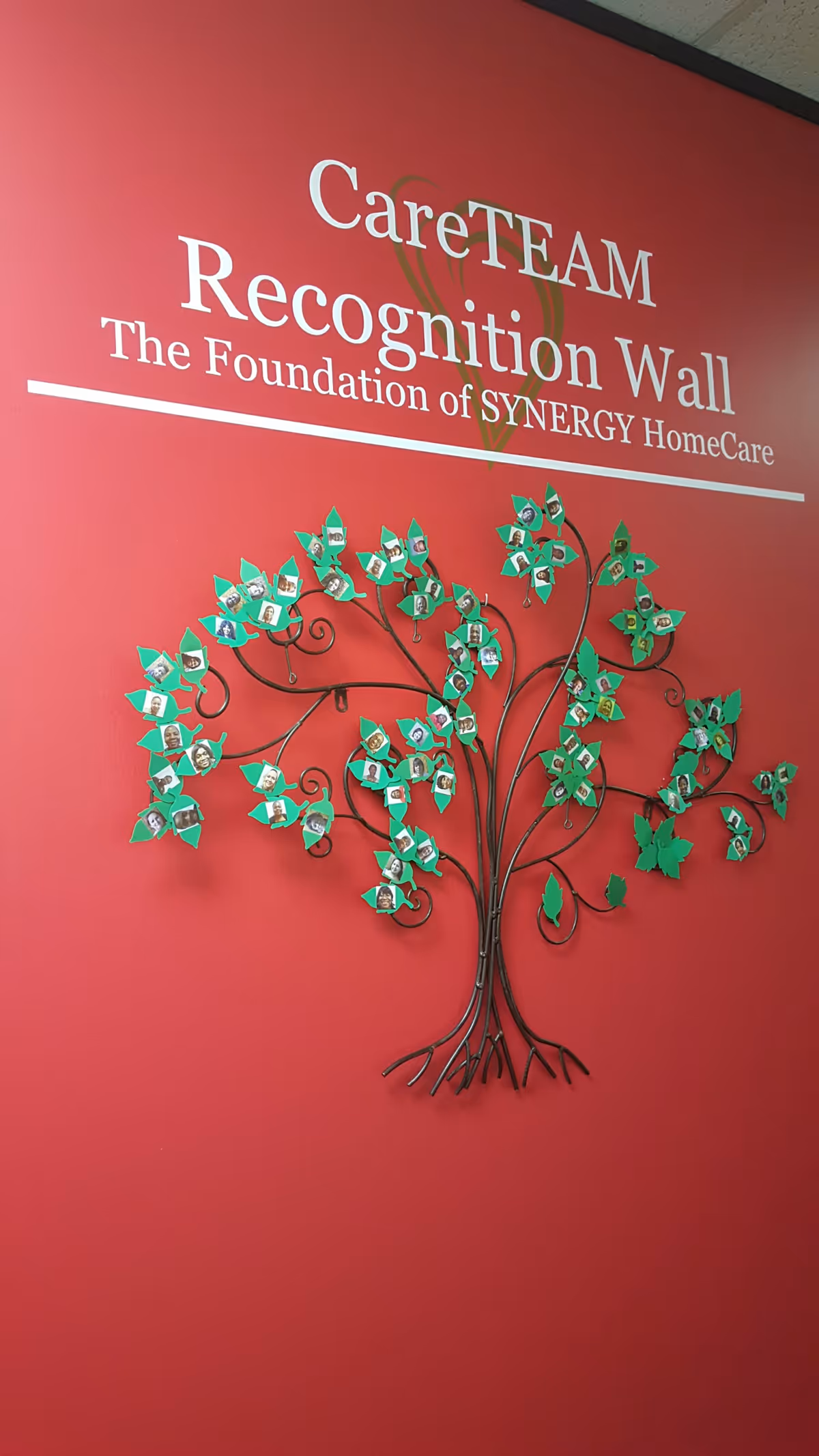 Red wall featuring CareTEAM Recognition Wall and a decorative metal tree with photo leaves.