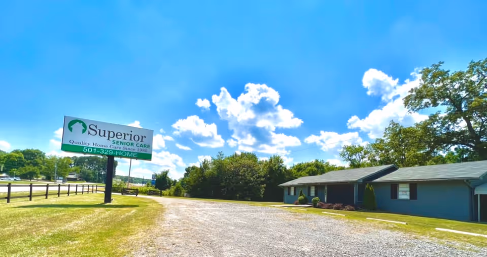 Front view of a blue, single-story senior care facility with a roadside sign.