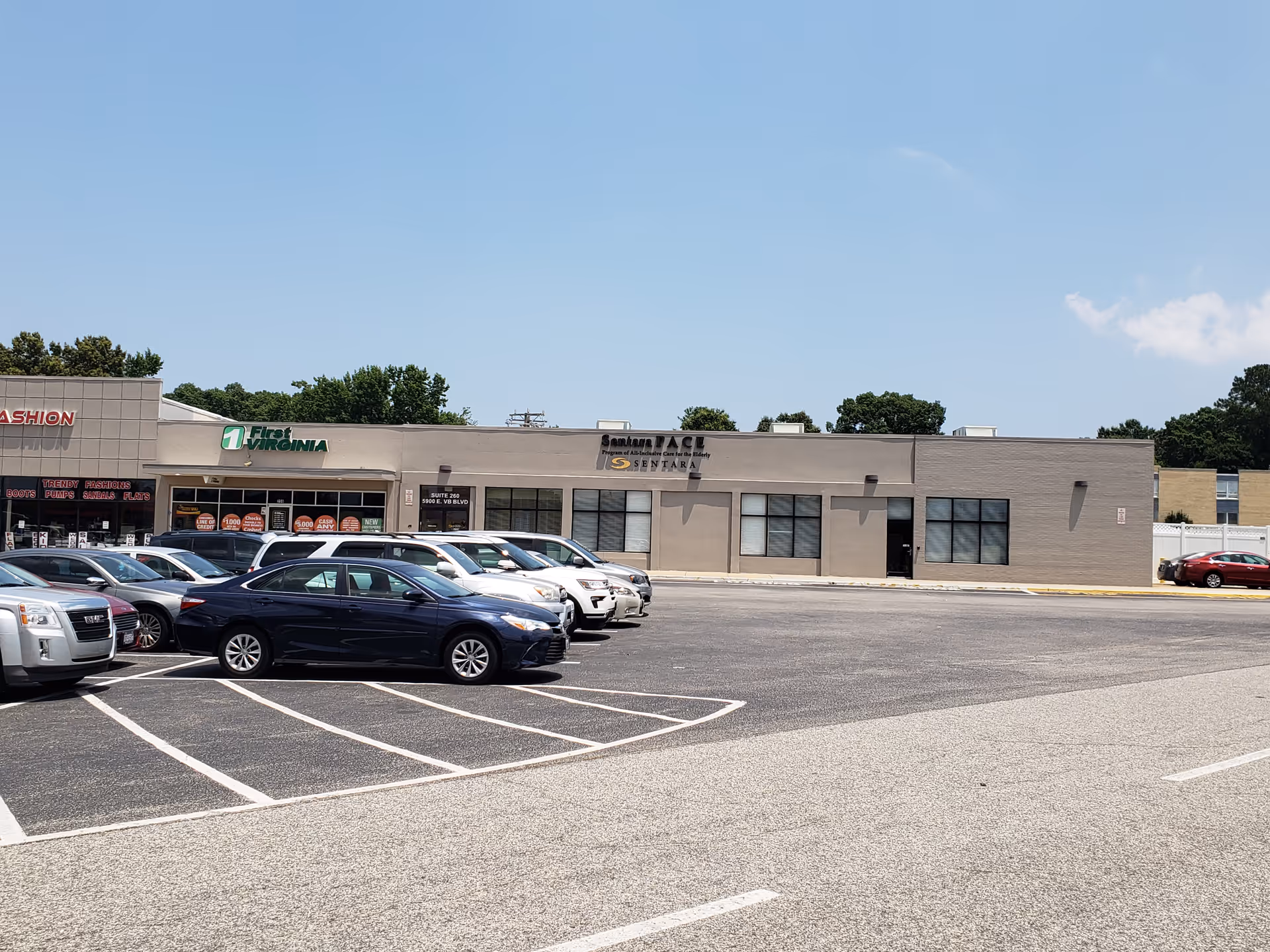 Empty parking lot in front of a row of storefronts under clear blue sky.