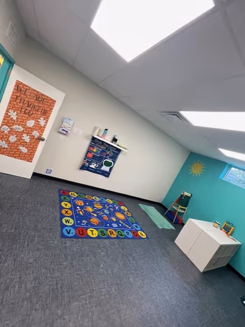 An empty autism therapy room with alphabet rug, teal walls, and storage cubes.
