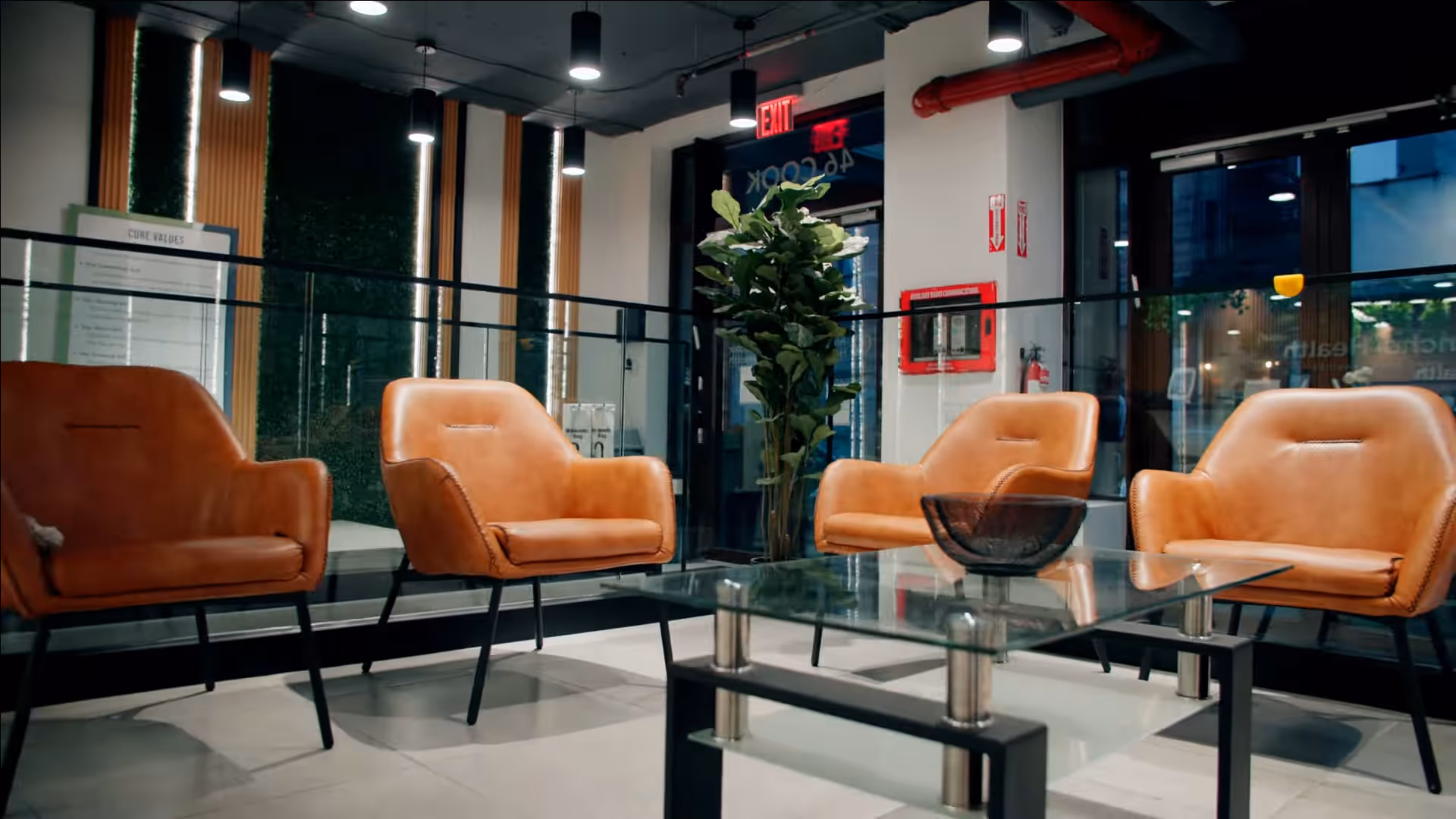 Modern indoor lounge with orange leather armchairs around a glass coffee table.