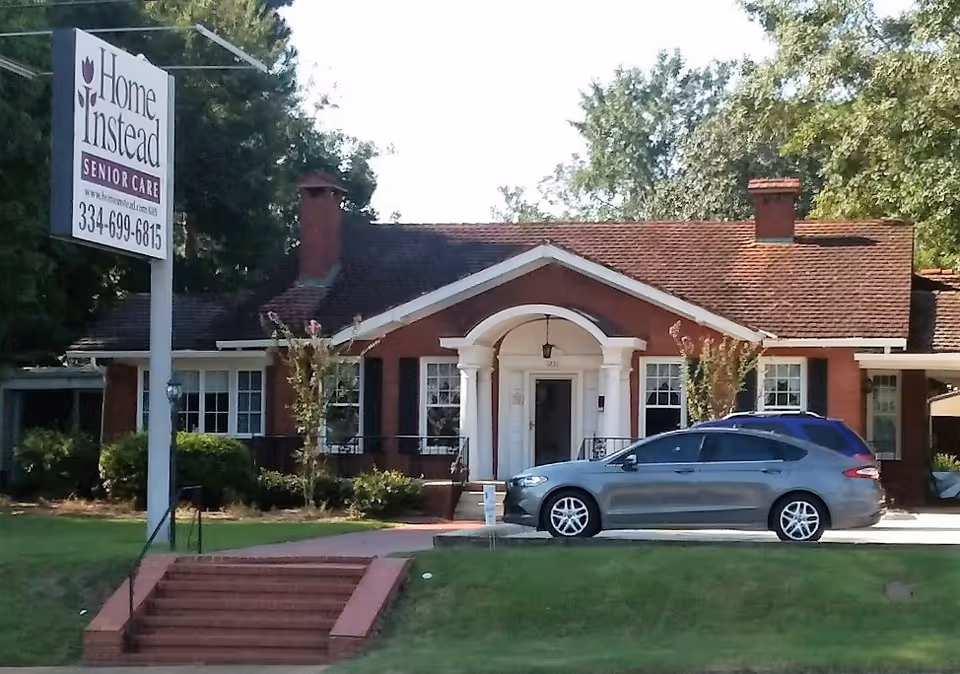 Brick senior care facility with a Home Instead sign and a gray car in the driveway.