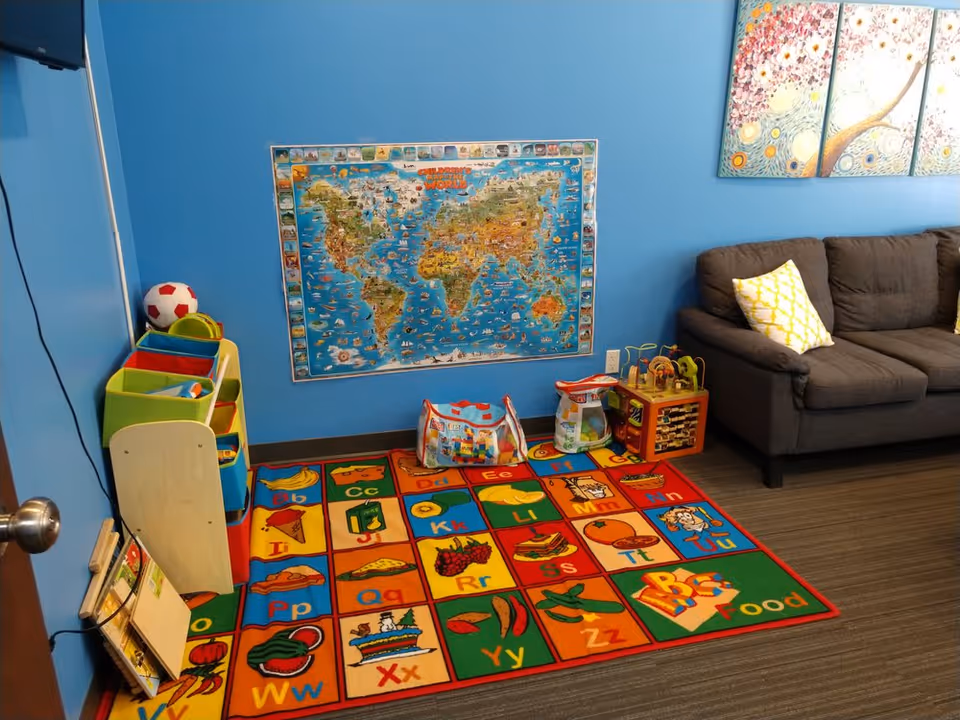 Bright blue playroom with map, colorful alphabet rug, toy storage, and a gray sofa.