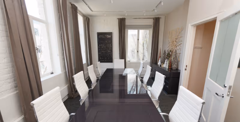 Bright dining room with a long glass table and white chairs by windows with curtains.