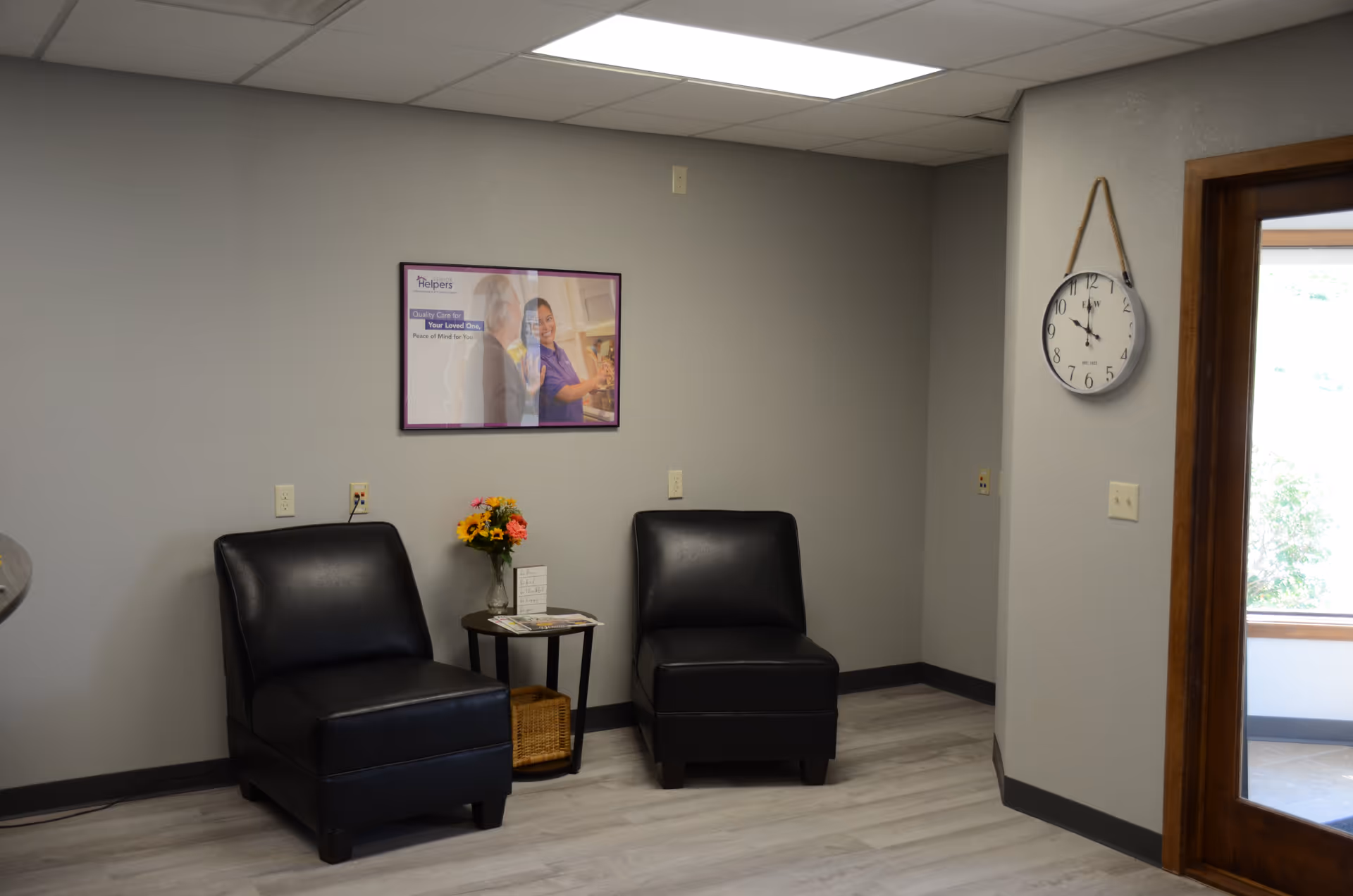 Two black leather chairs face a small table with flowers in a waiting area.