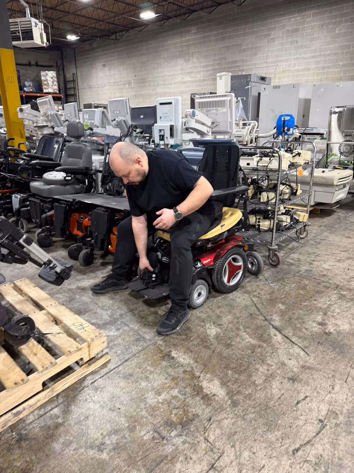 Man in a wheelchair inspects a warehouse filled with hospital beds and medical equipment.