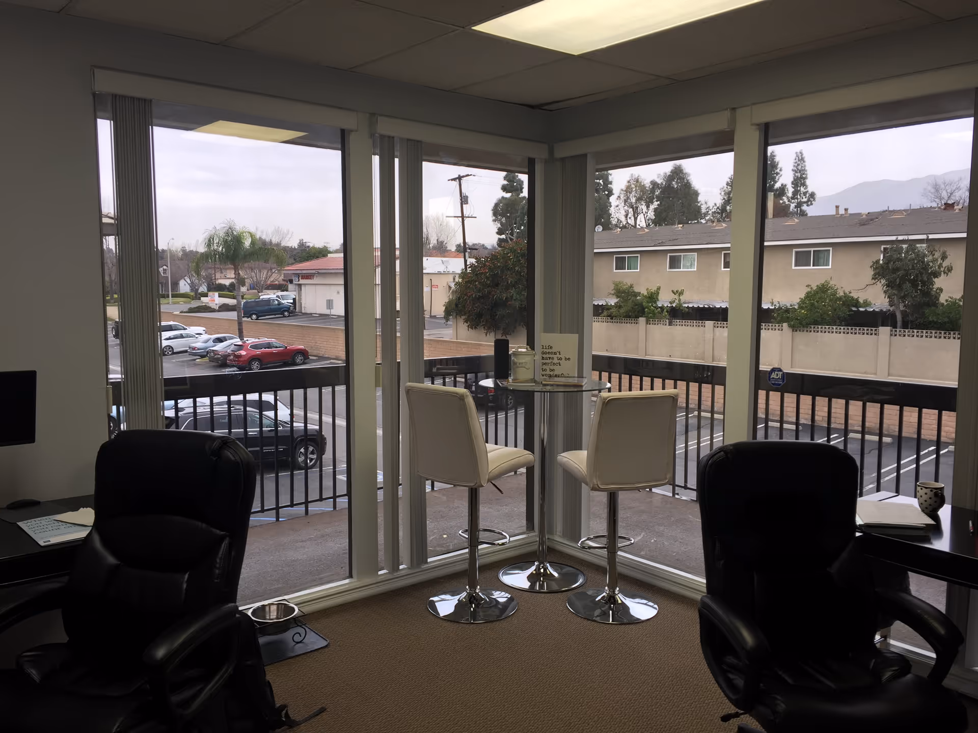 Interior lounge with large windows, a round glass table, and white bar stools.