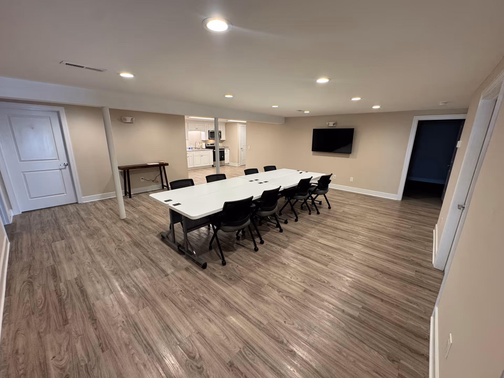 A large conference room with a long white table, black chairs, and a wall-mounted TV.