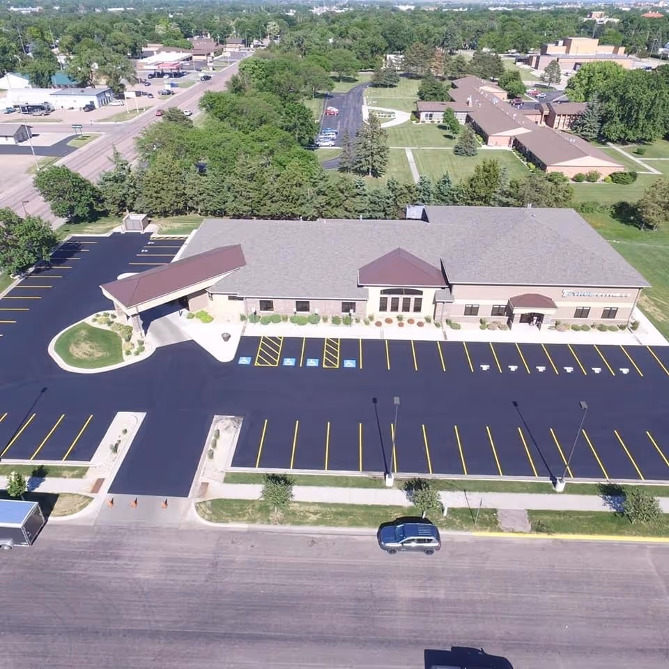 Aerial view of a single-story medical facility with large parking lot and landscaped surroundings.