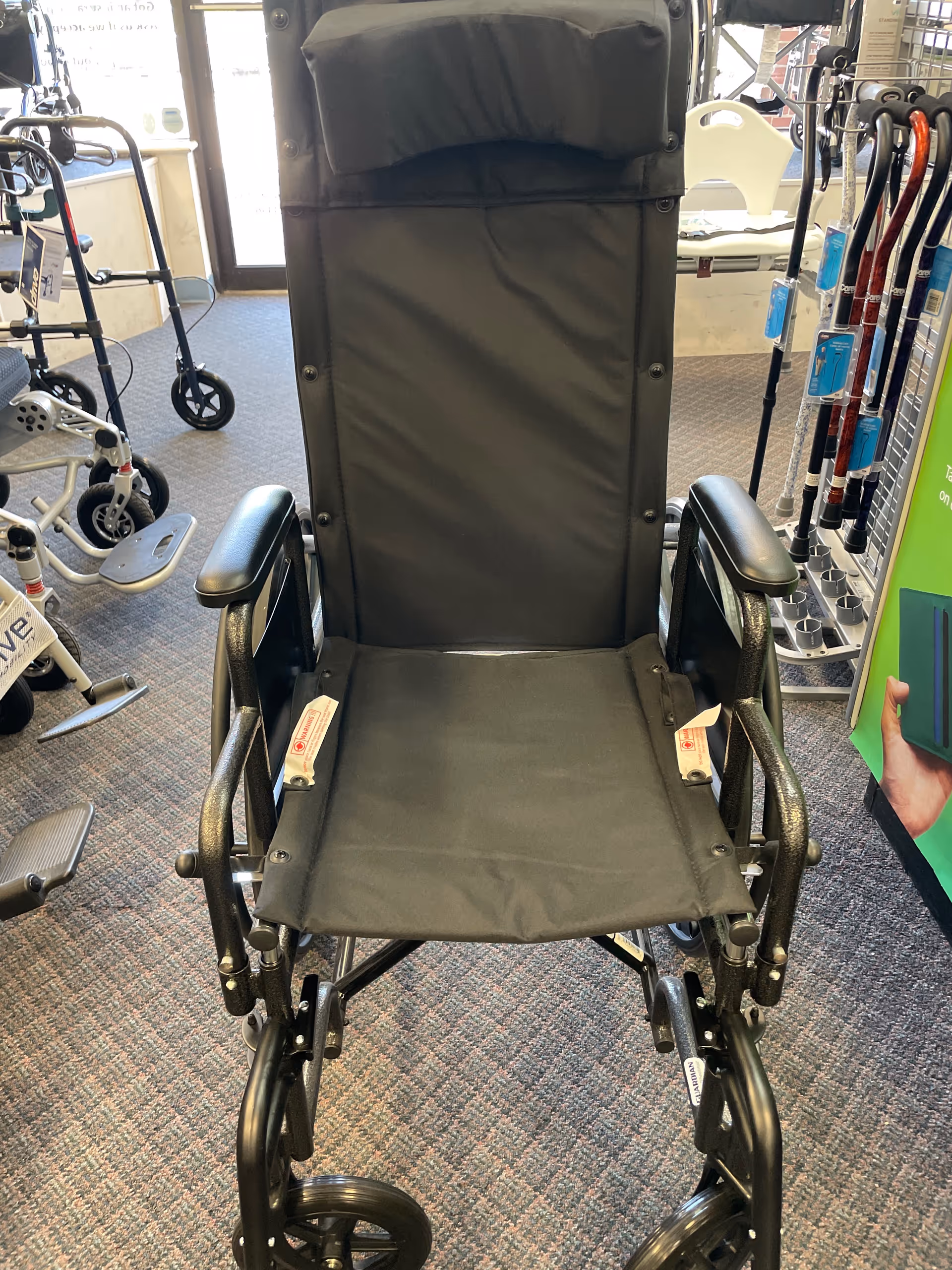Black wheelchair displayed in an interior showroom with walkers and mobility aids.
