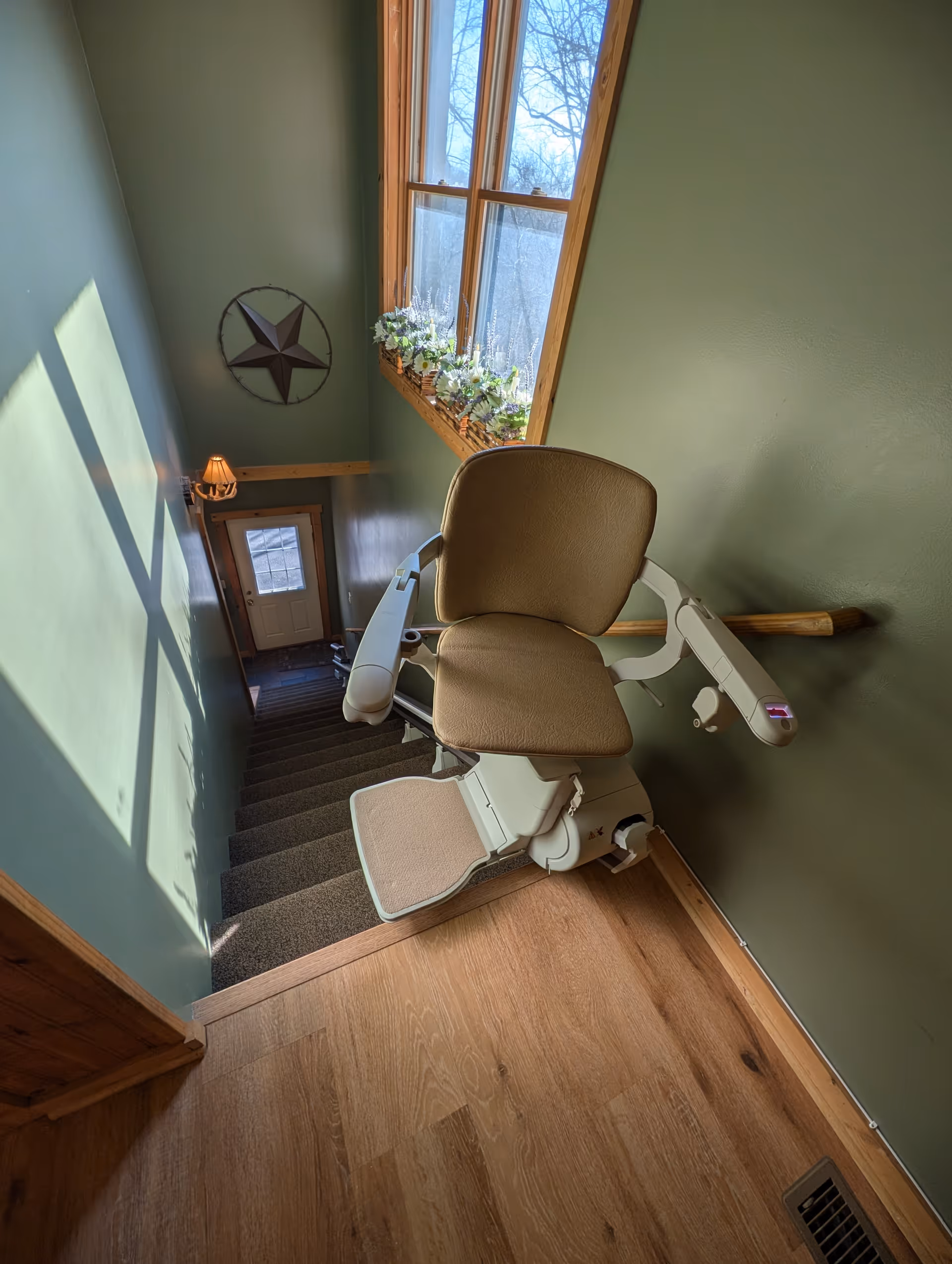 Green-walled stairway with a beige stair lift chair by a window and door.
