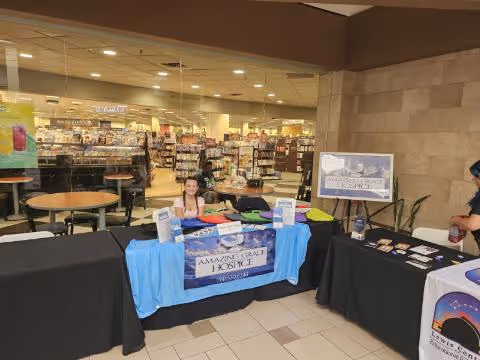 Inside a mall-like facility, hospice booth with staff at a blue-covered table.