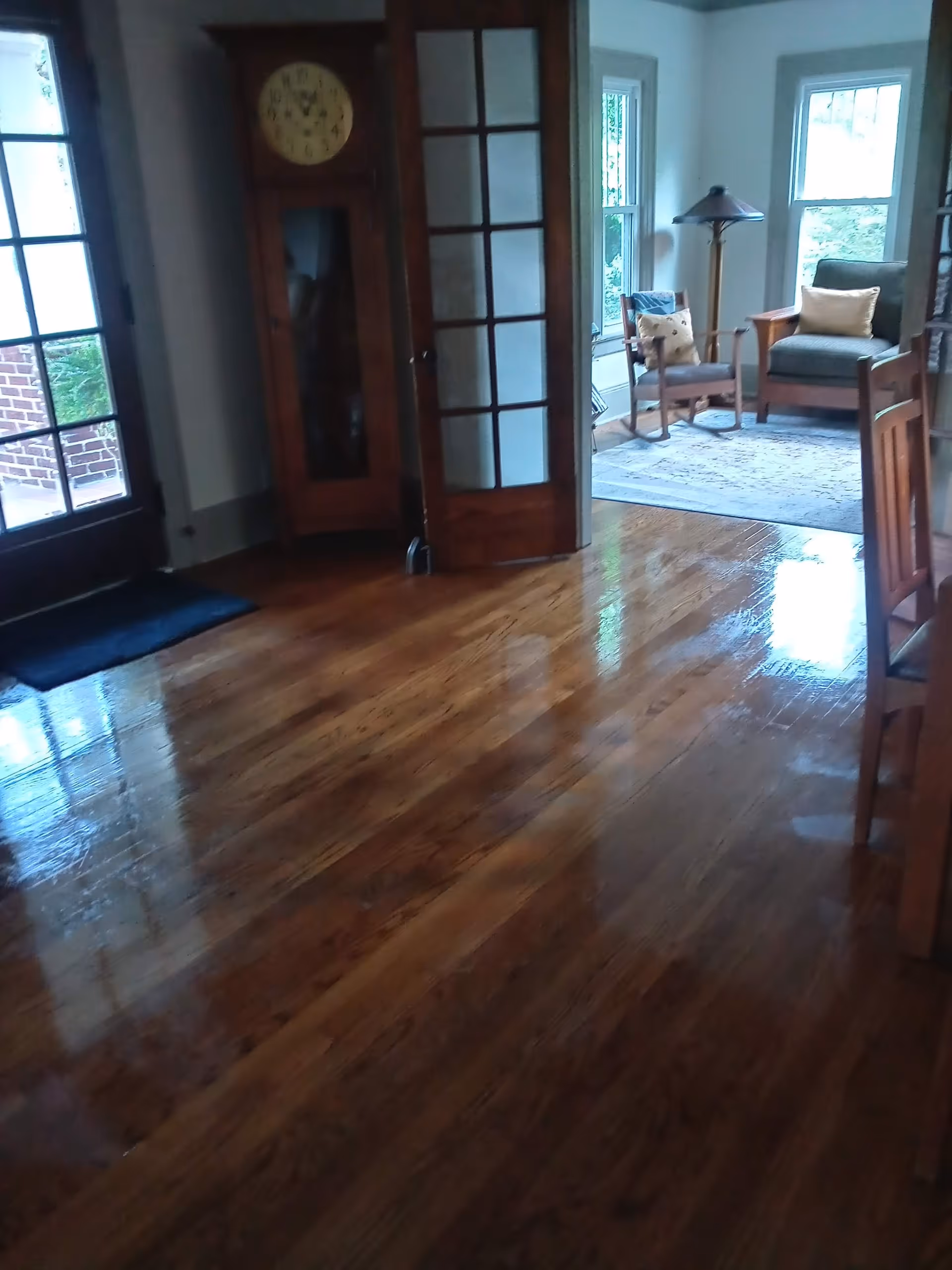 Polished wooden floor leads to a sunlit seating area with a grandfather clock.
