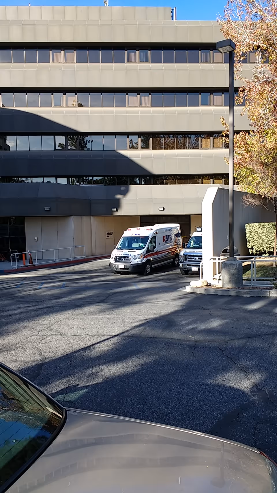 Exterior view of a multi-story hospital with ambulances parked in front.