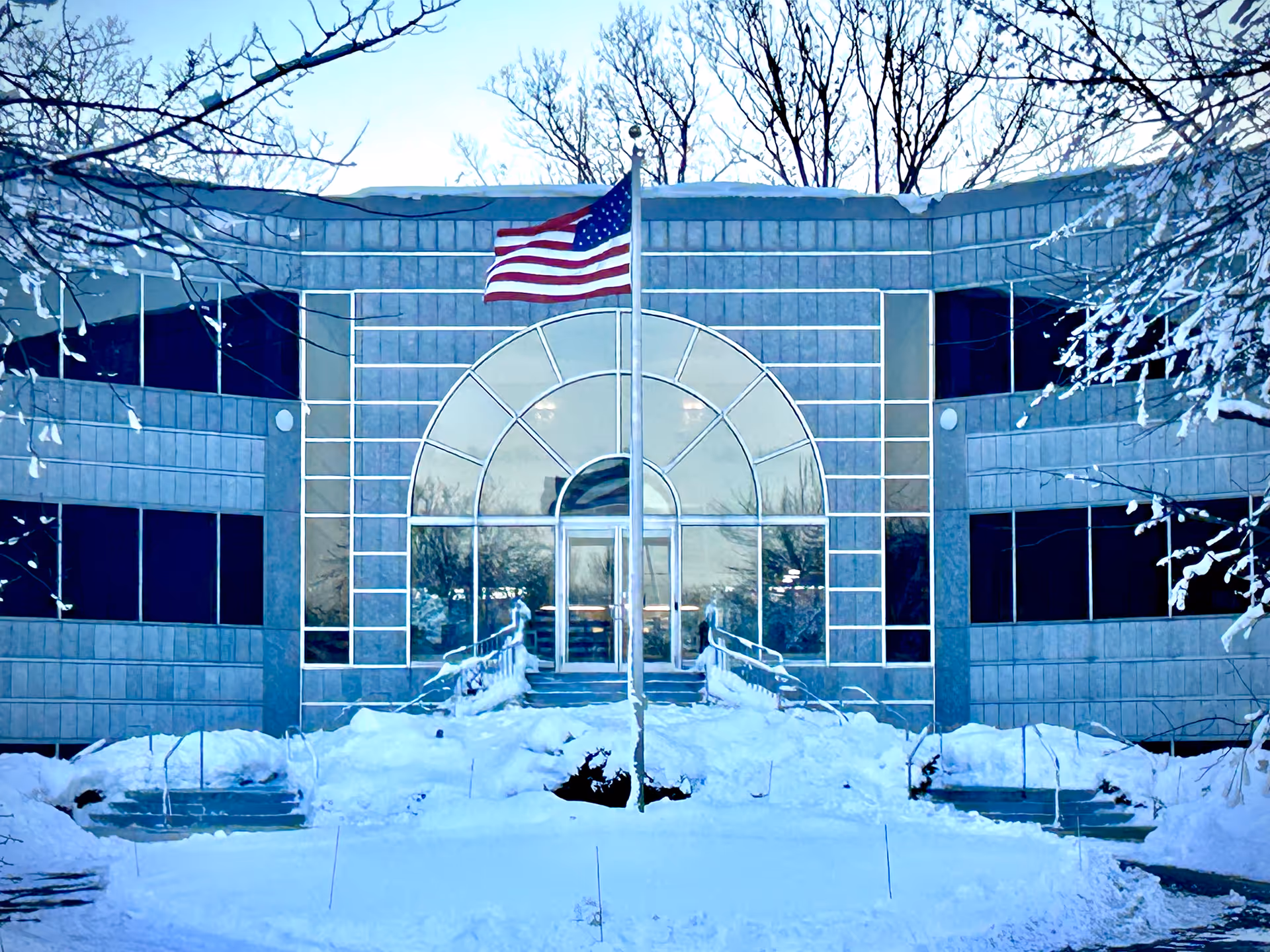A snowy daytime view of the Aveanna Home Health building front with an arched glass entrance.