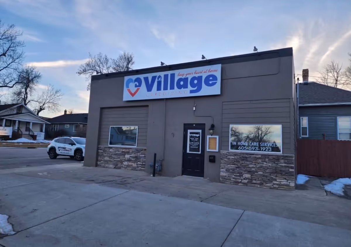 Exterior view of Village Caregiving building with large sign, door entrance, and parked car nearby.