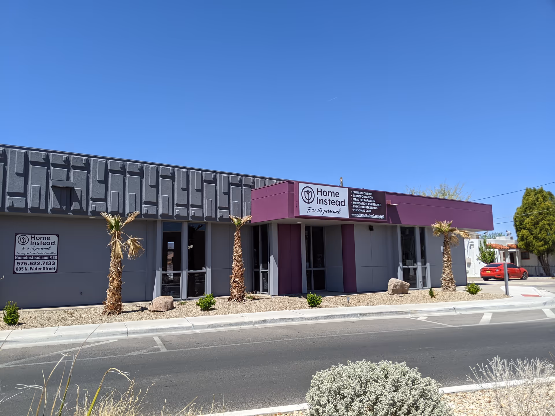 Front exterior of a Home Instead facility with a purple sign and palm trees.