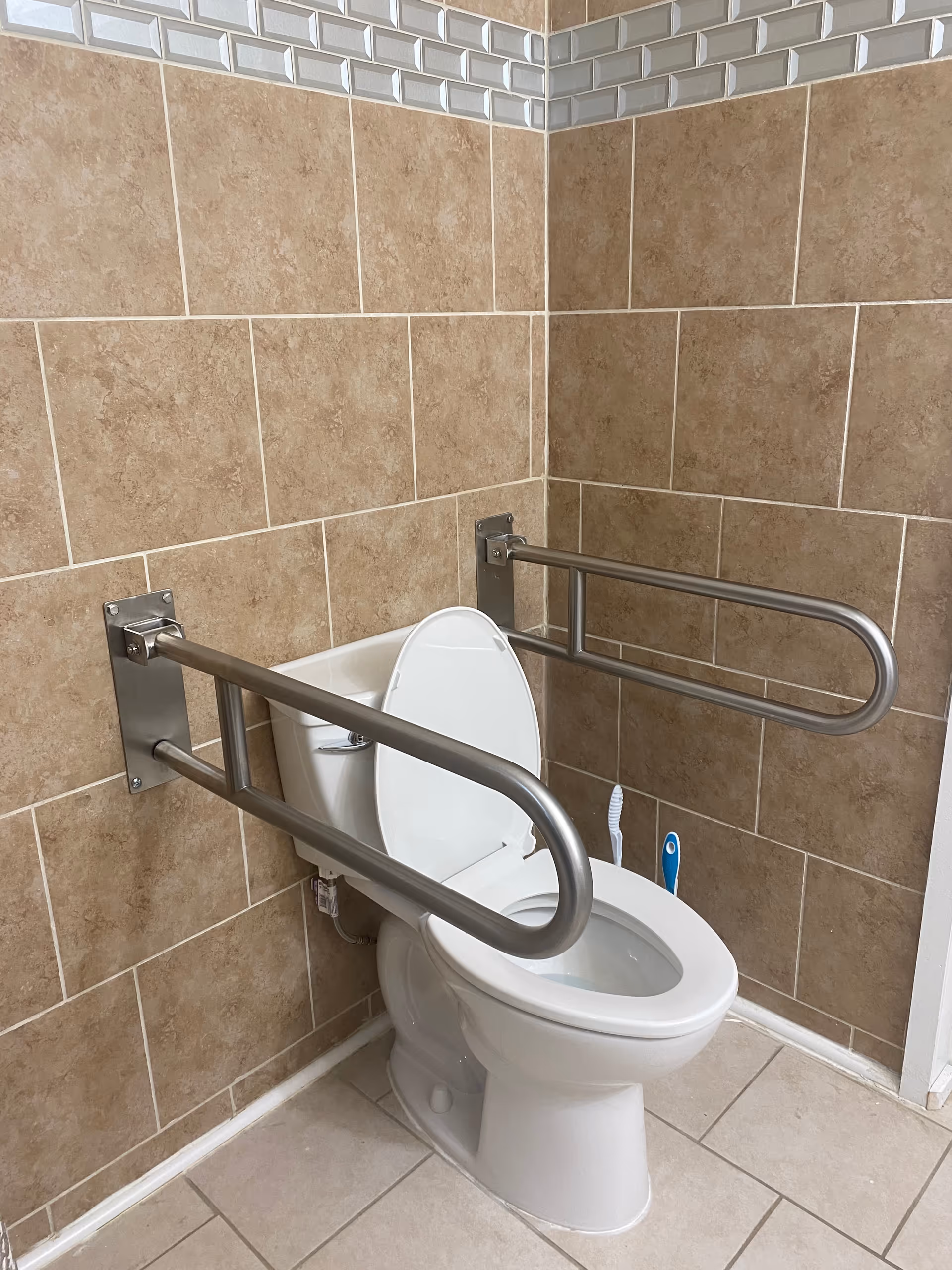 Accessible bathroom featuring a toilet with wall-mounted grab bars and tiled walls.