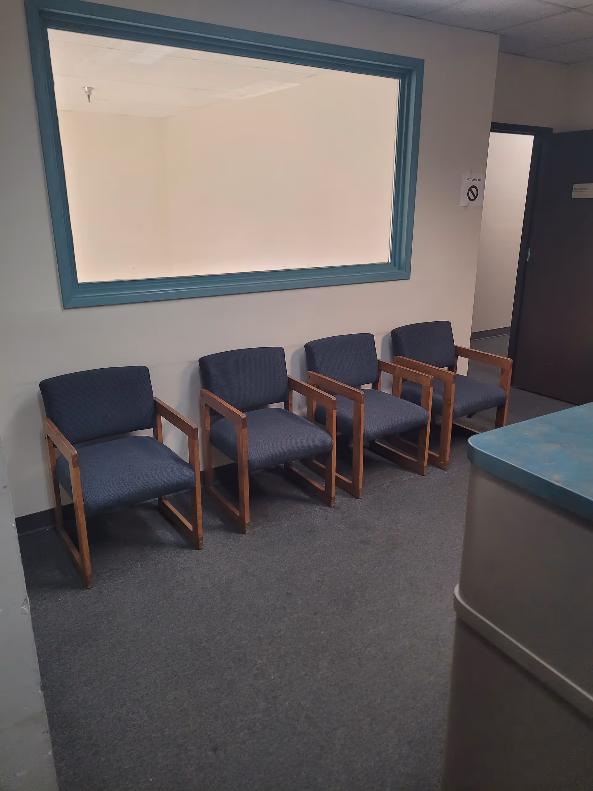 Five blue upholstered chairs line the wall in a small facility waiting area.
