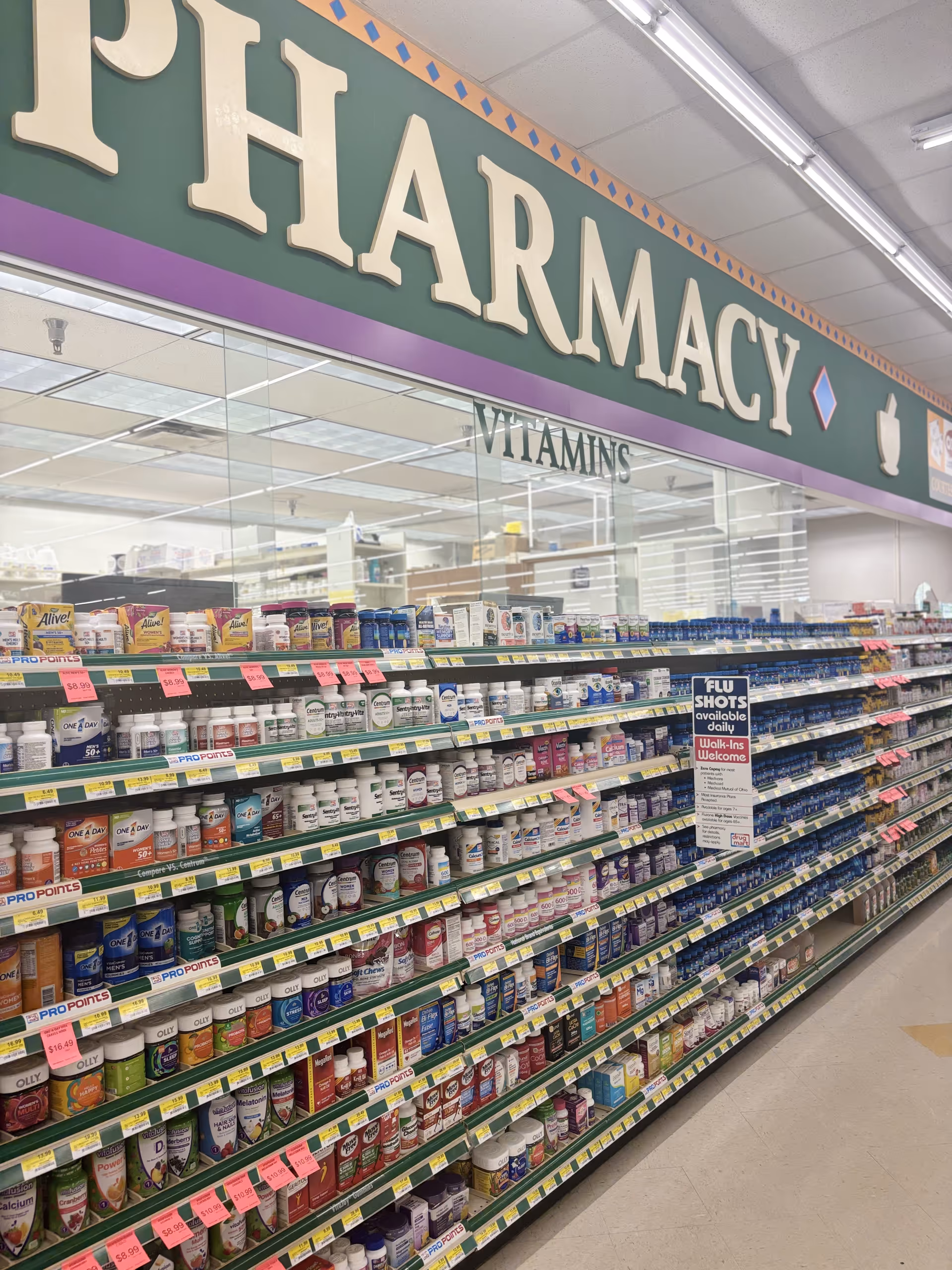 Interior of Discount Drug Mart pharmacy aisle with vitamin shelves and signage.