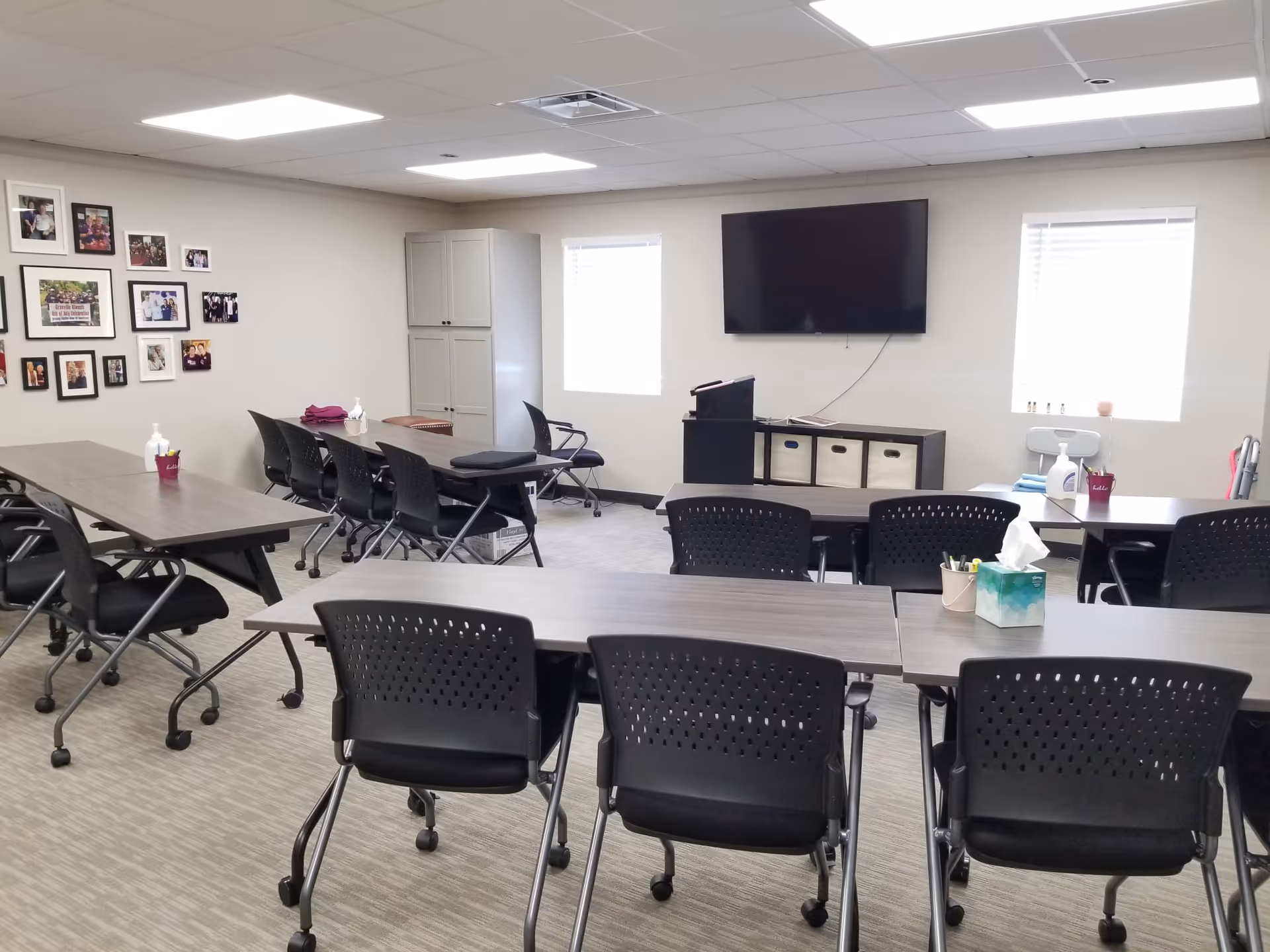 Multipurpose senior living common room with tables, chairs, and a wall photo collage.