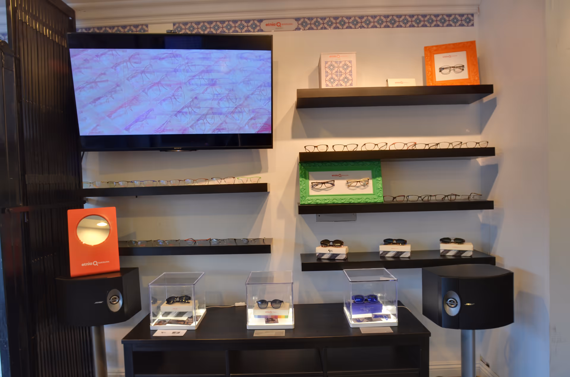 Interior eyewear showroom with shelves of glasses, a wall-mounted TV, and glass display cases.
